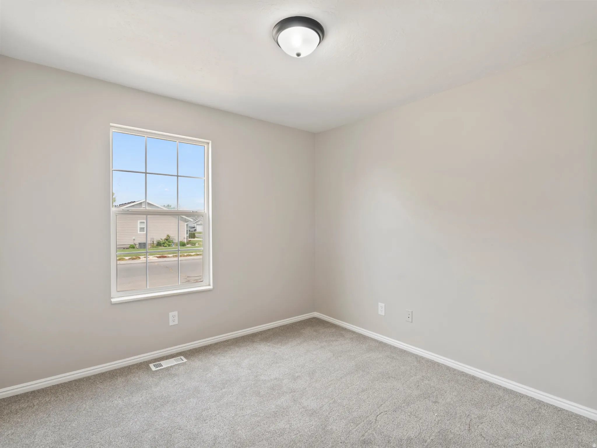 Neutral-toned room featuring a single-pane window with grid inserts, gray carpeting, white baseboards, and a flush-mount ceiling light fixture