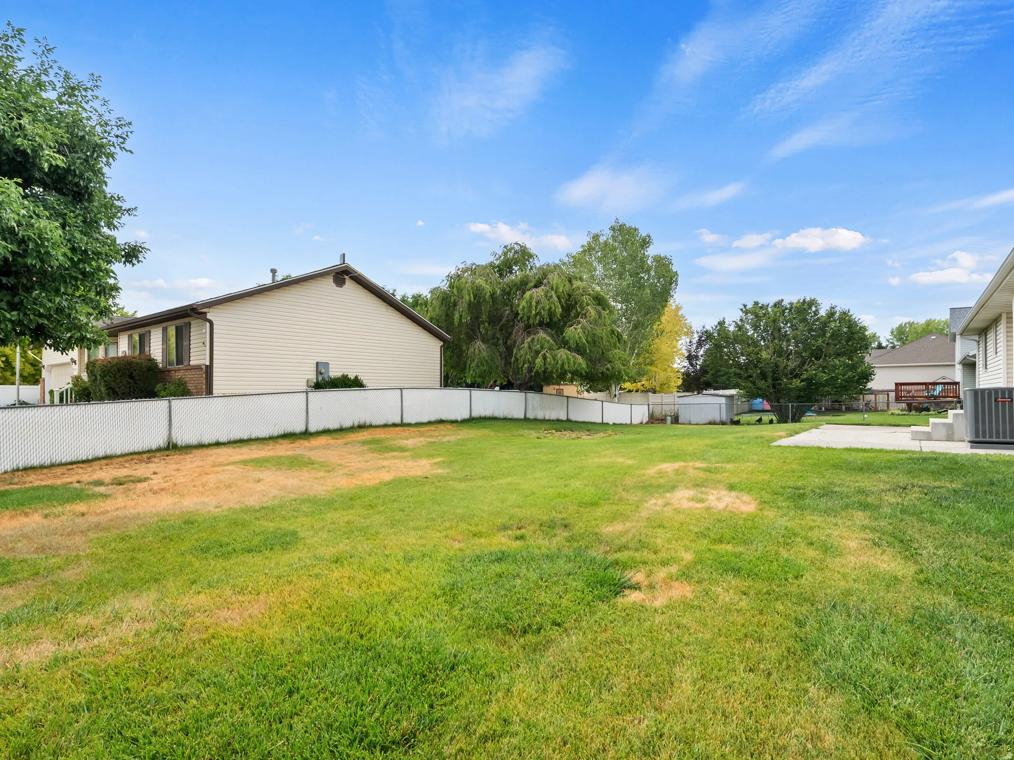Expansive rear yard featuring a large grass area, chain-link fence, and mature trees