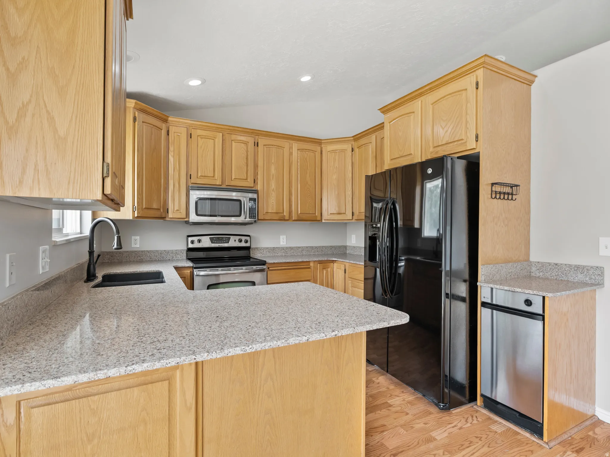 Well-appointed kitchen featuring light wood cabinetry, stone-finish countertops, and wood-finish flooring