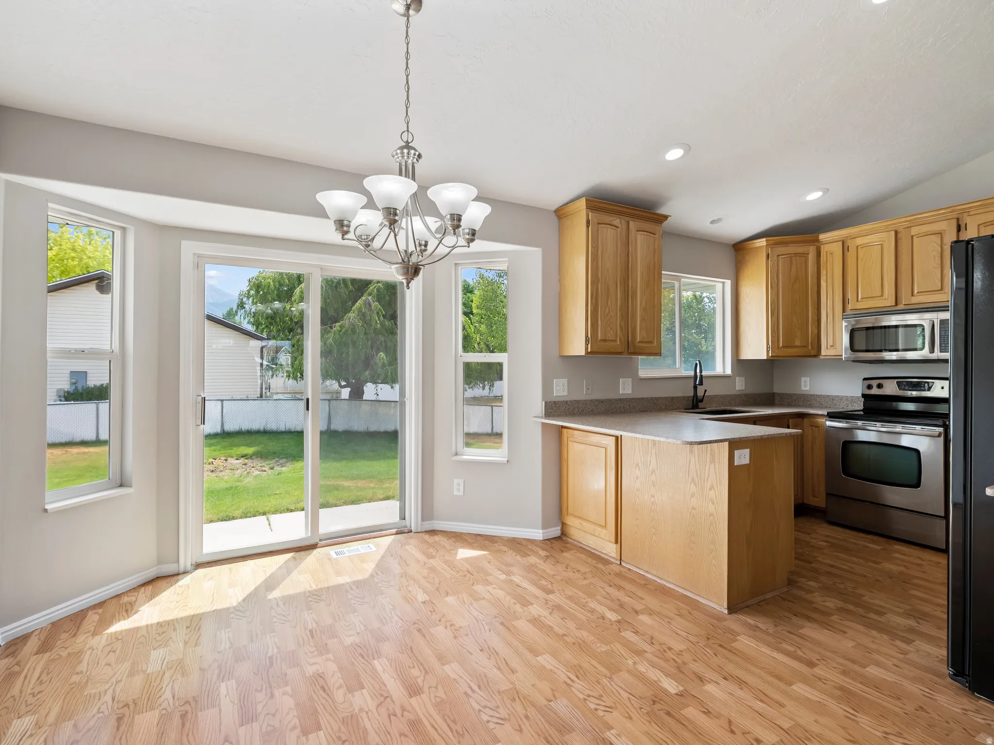 Open concept kitchen and dining area featuring wood-finish flooring, a contemporary chandelier, a kitchen island, and stainless steel appliances