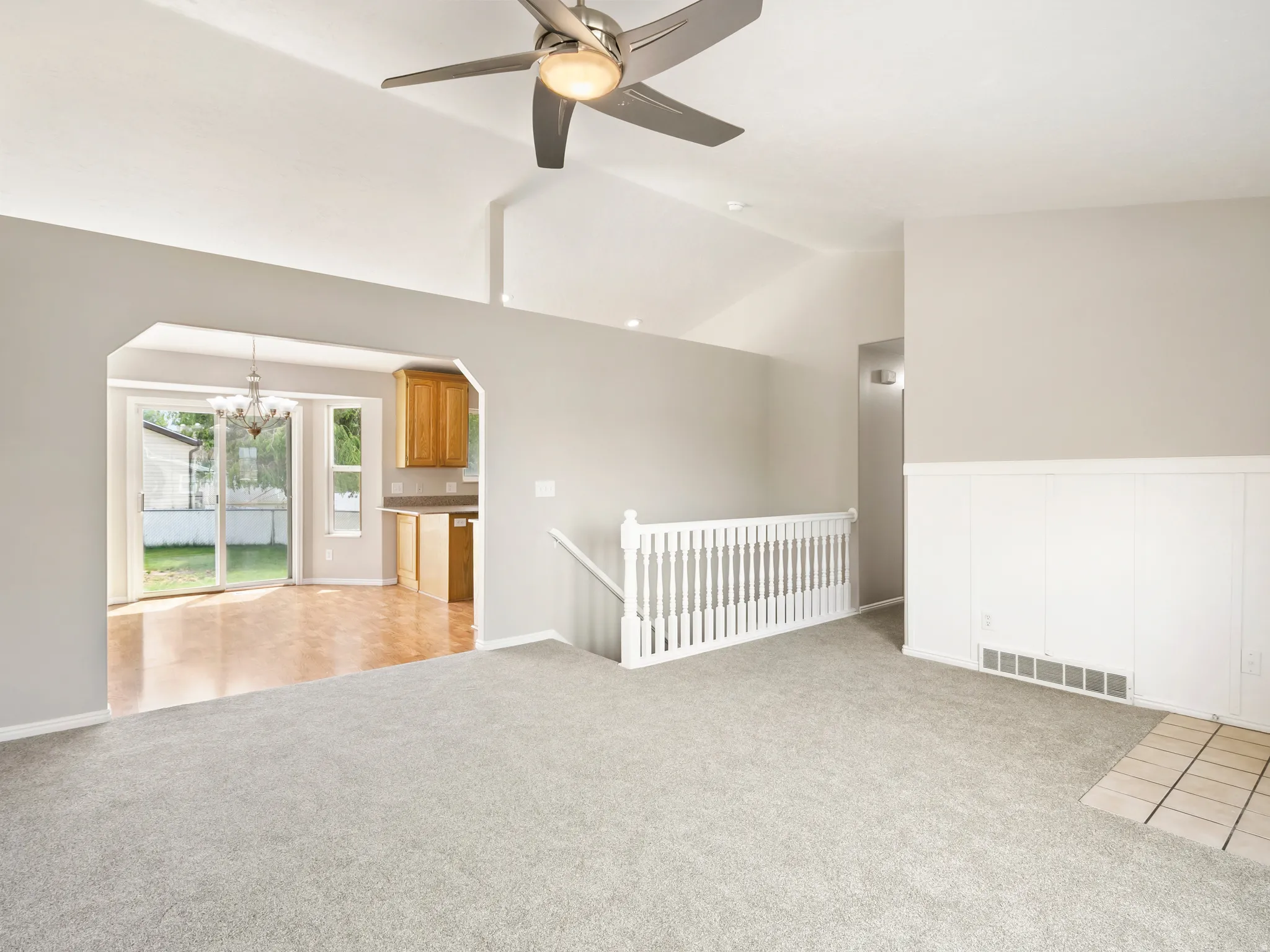 Vaulted ceiling living area featuring light gray carpeting, a contemporary ceiling fan, and white wainscoting