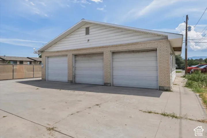 Three-car detached garage with roll-up doors, light brick siding, and a white gable roof