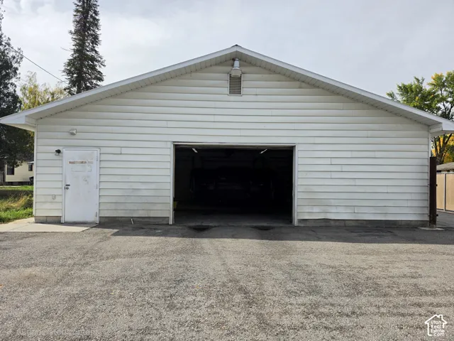 Detached garage featuring white horizontal siding, a gabled roofline, an exterior service door, and paved driveway access