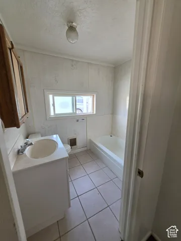 Bathroom featuring a white vanity cabinet, integrated sink, tiled flooring, built-in tub, and a flush-mount ceiling light fixture