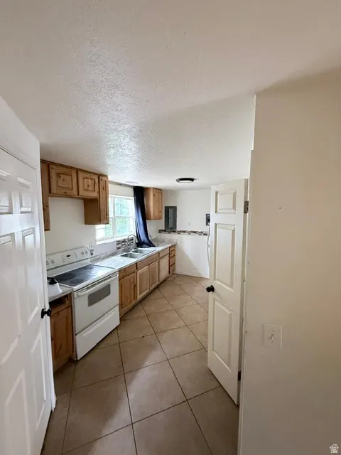 Kitchen featuring light wood-finish cabinetry, tile flooring, white electric range, and double basin sink