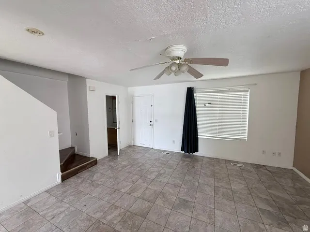 Interior space featuring neutral-toned tile flooring, a ceiling fan with integrated lighting, and a white paneled door