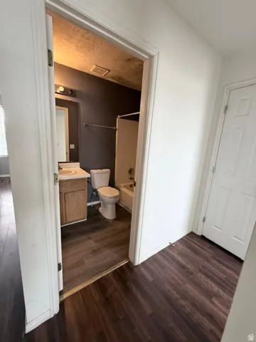 Bathroom featuring wood-finish flooring, a vanity with a light wood-tone cabinet, a toilet, and a bathtub with shower