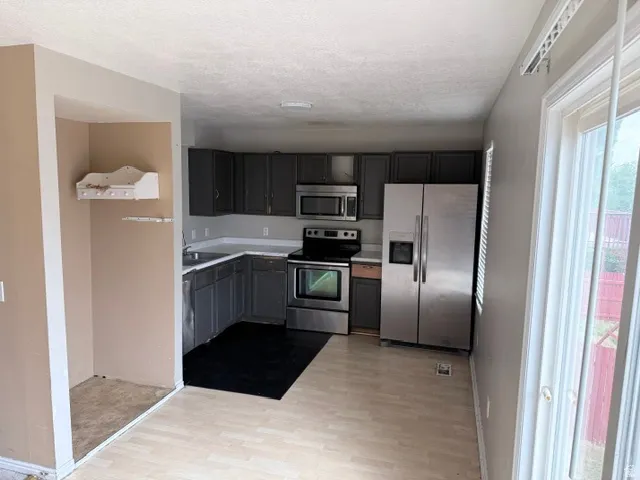 Kitchen featuring dark cabinetry, stainless steel appliances, light countertops, and wood-finish flooring