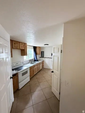 Kitchen featuring light wood-finish cabinetry, tile flooring, white electric range, and double basin sink
