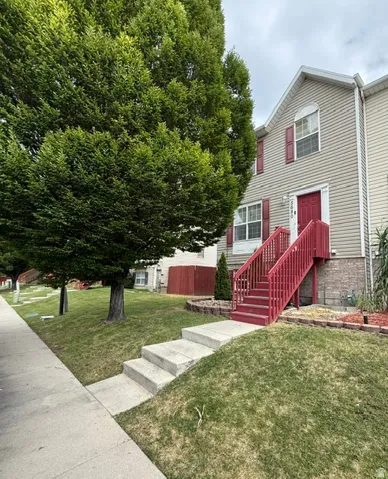 Two-story exterior featuring tan siding, red window shutters, and a prominent red stairway leading to the main entrance