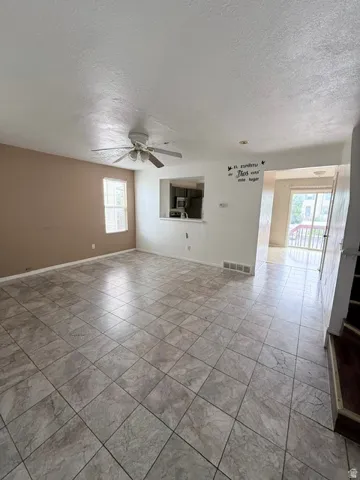 Spacious living area featuring large format tile flooring, a ceiling fan with integrated lighting, and a pass-through opening to the kitchen