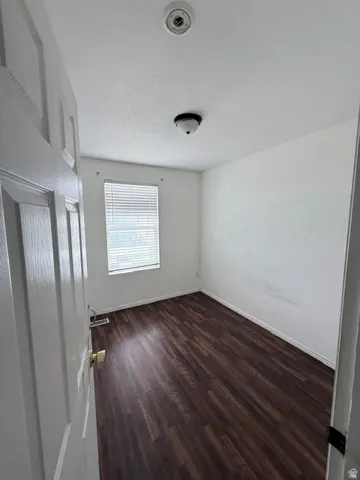 Interior room featuring wood-finish flooring, white walls, and a window with horizontal blinds