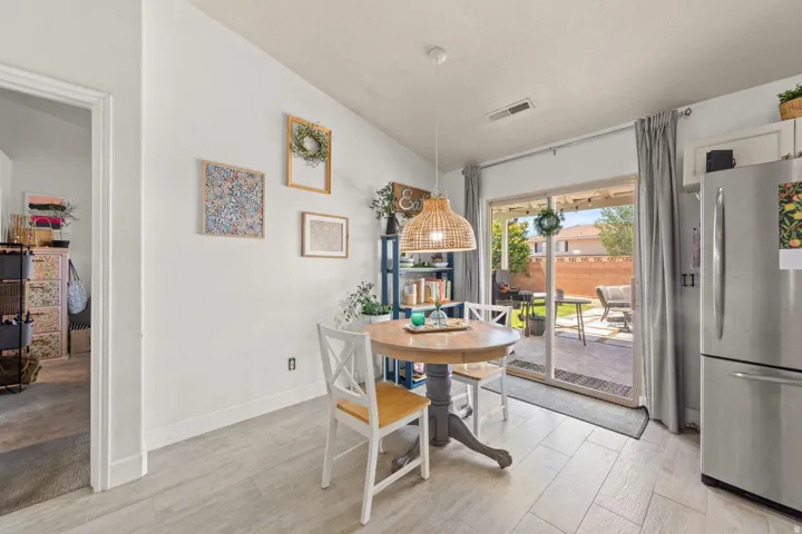 Kitchen dining area featuring light wood-finish flooring, a contemporary pendant light fixture, and a sliding glass door leading to a paved patio