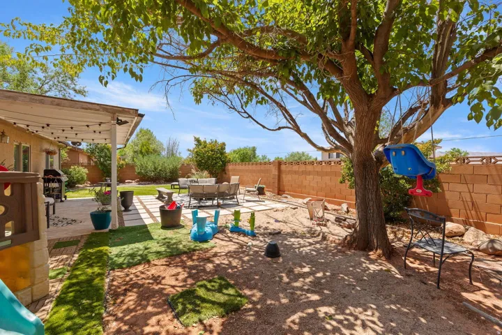 Expansive backyard featuring a mature shade tree, a covered patio with string lighting, a concrete patio area, and a block fence perimeter