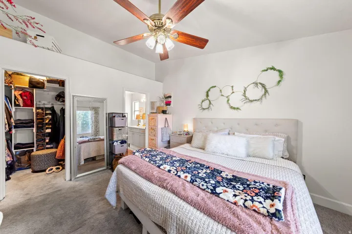 Spacious bedroom featuring vaulted ceilings with a ceiling fan, plush carpet flooring, and a walk-in closet with built-in shelving