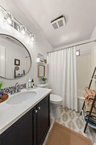 Bathroom featuring a dark wood-finish vanity with a white countertop and oval sink, a round wall-mounted mirror, a tiled backsplash, and a tub with a shower curtain