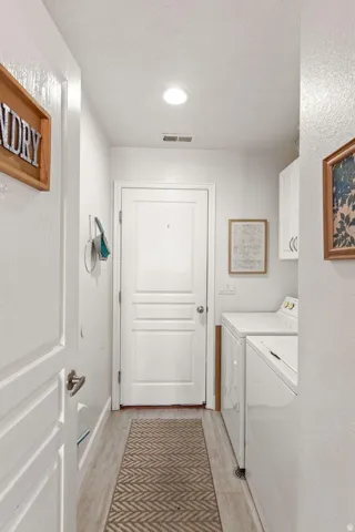 Dedicated laundry area featuring wood-finish flooring, recessed lighting, and a built-in wall cabinet