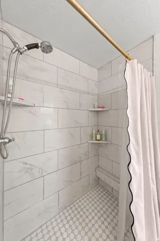 Tiled shower featuring a handheld showerhead, white subway tile walls, hexagonal floor tiles, a built-in bench, and corner shelving