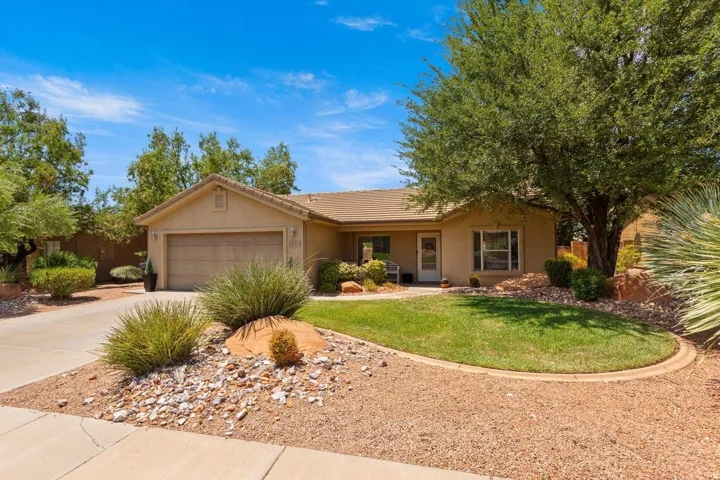 Single-story stucco residence featuring an attached garage, a xeriscaped front yard with mature plantings, and a concrete driveway