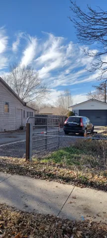 Gated gravel driveway leading to a detached two-car garage with a roll-up door
