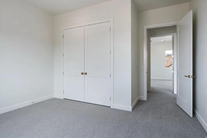 Neutral-toned room featuring a closet with bi-fold doors and golden hardware, light gray carpet, and white baseboards