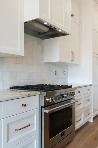 Stainless steel range with a gas cooktop, under-cabinet range hood with integrated lighting, and white shaker-style cabinetry with gold-tone hardware
