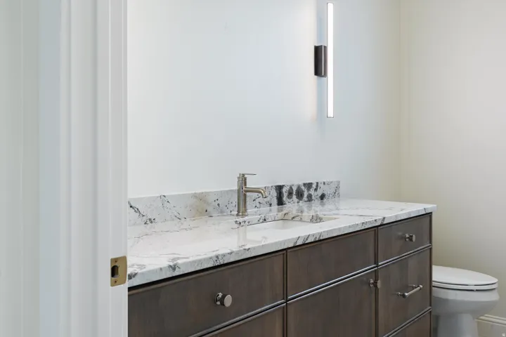 Vanity featuring a stone countertop with an integrated sink, brushed nickel faucet, and linear wall sconce