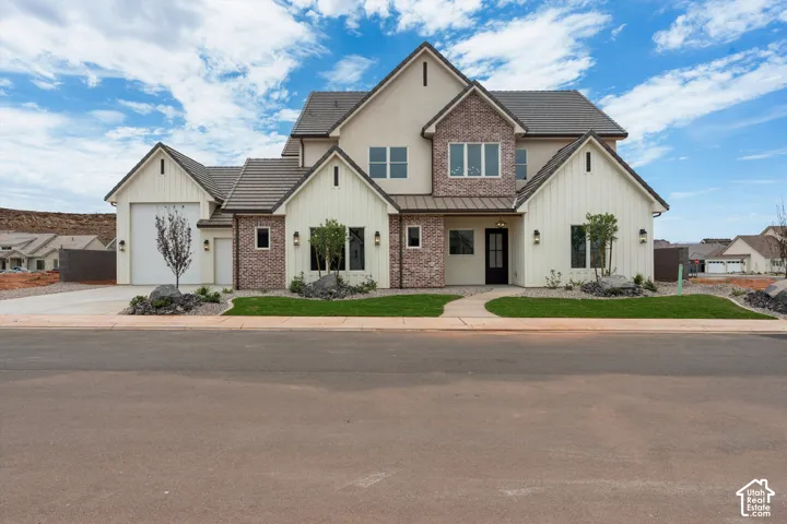Contemporary exterior featuring board and batten siding, brick accents, stucco finishes, a dark tile roof, and a two-car garage