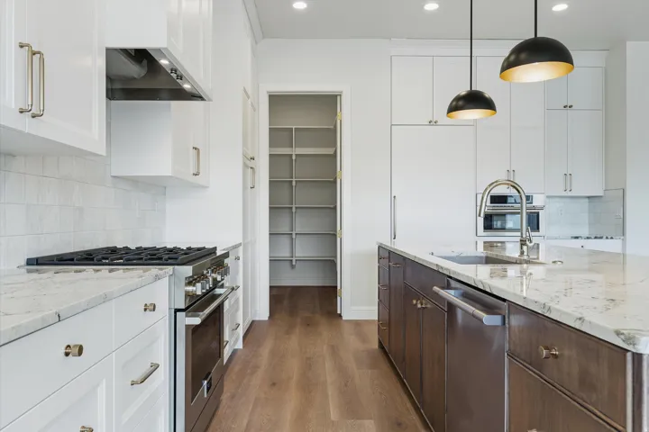 Kitchen featuring stainless steel appliances, an integrated refrigerator, an eat-at island with a sink, pendant lighting, and a walk-in pantry