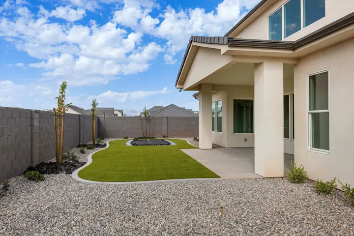 Expansive backyard featuring a covered patio with concrete flooring, artificial turf, gravel landscaping, and a privacy block wall