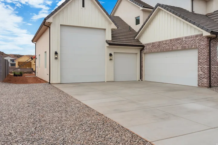 Exterior featuring three white garage doors, a concrete driveway, board and batten siding, brick accents, and a tile roof