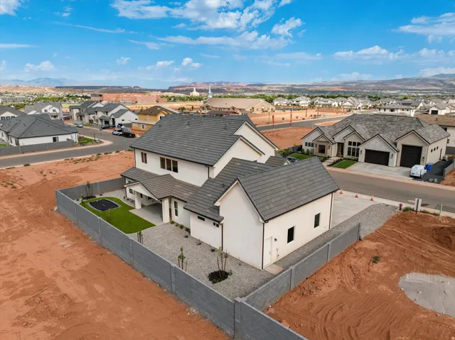 White stucco exterior, gray tile roofing, enclosed backyard with a manicured lawn, attached covered patio, and a dedicated side entrance