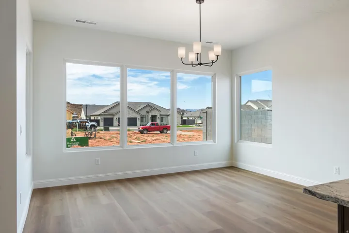 Spacious interior room featuring multiple large windows, wood-finish flooring, and a contemporary chandelier