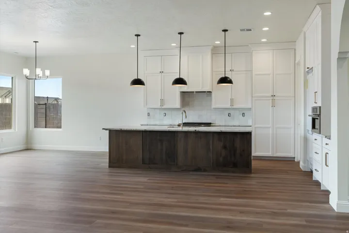 Modern kitchen featuring a large island with a stone countertop, white shaker-style cabinetry, a white subway tile backsplash, and stainless steel built-in appliances