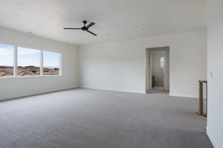 Spacious room featuring three large windows, gray patterned carpeting, a matte black ceiling fan, recessed lighting, and a white interior door