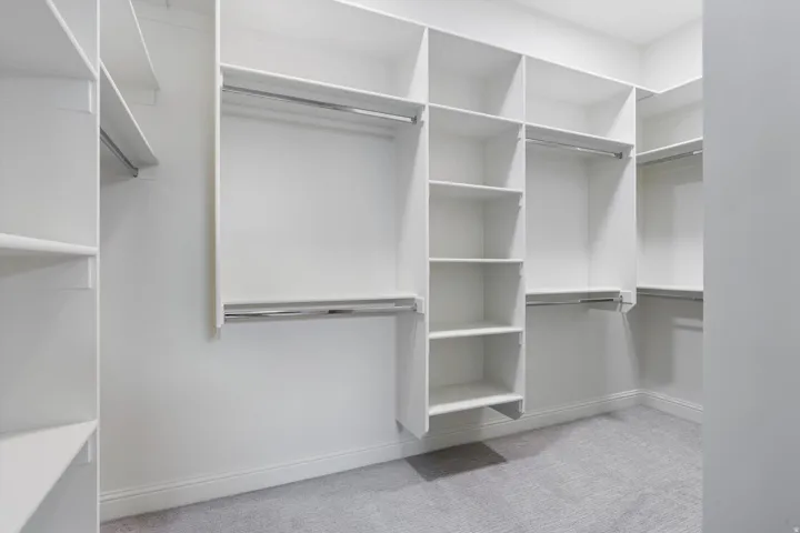 Walk-in closet featuring white built-in shelving, multiple hanging rods, and light gray carpeting