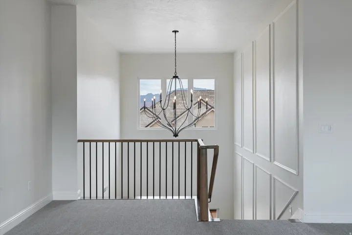 Second-story landing featuring a wrought iron chandelier, window with mountain backdrop, panel molding detail, wood-finish handrail, and gray carpeting