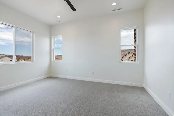 Bright room featuring light gray carpeting, crisp white walls, multiple windows providing ample natural light, recessed ceiling lights, and a modern black ceiling fan