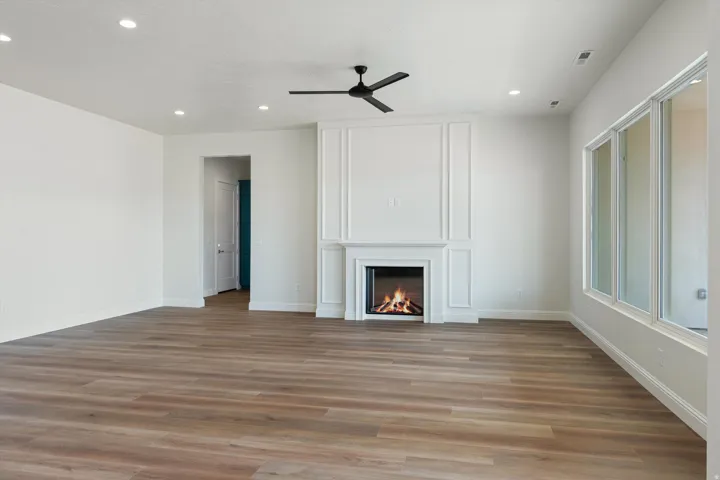 Living area with a fireplace featuring decorative paneling, wood-finish flooring, recessed lighting, and a contemporary ceiling fan
