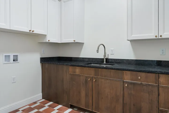Utility room featuring wood-finish lower cabinetry, white upper cabinetry, and a dark stone countertop with an undermount sink