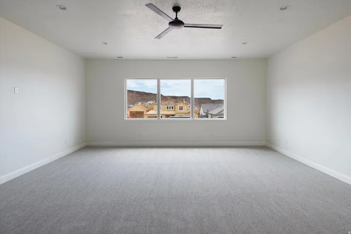 Spacious room featuring neutral carpeting, white walls, and a contemporary ceiling fan