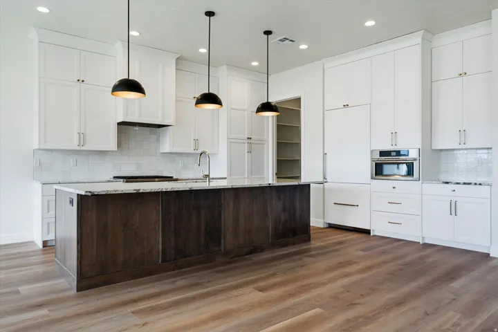 Kitchen featuring wood-finish flooring, a central island with a contrasting wood base, white shaker-style cabinetry, and integrated stainless steel appliances