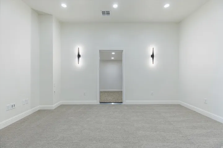 Recessed ceiling lighting, wall-mounted sconces, neutral carpet flooring, white walls, and white baseboards