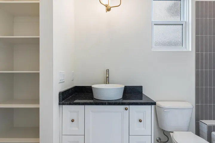 Vanity featuring a vessel sink with a dark stone countertop, white cabinetry with bronze hardware, and a single-handle faucet