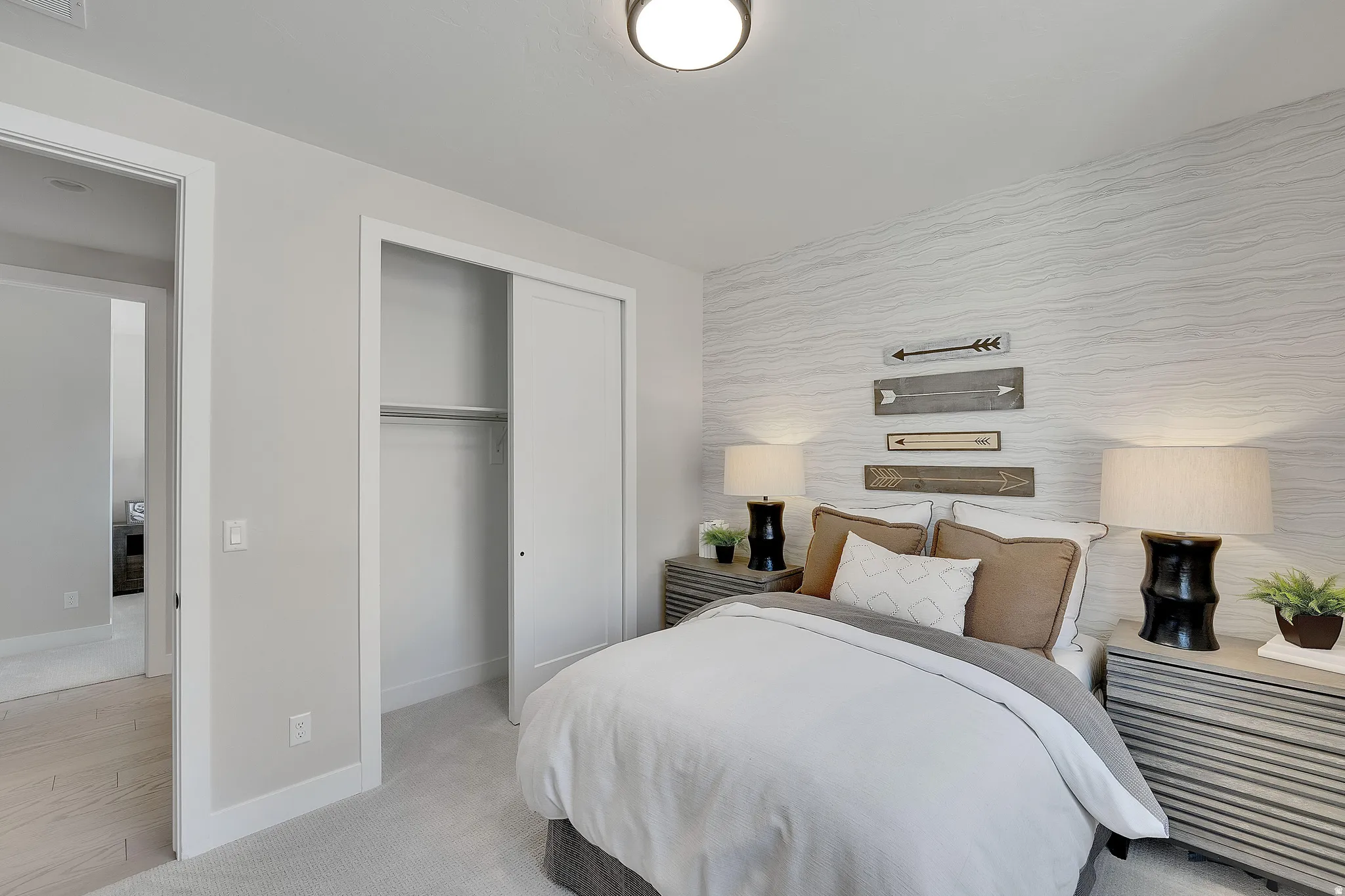 Bedroom featuring a patterned accent wall, light gray carpeting, and a built-in closet with sliding doors. This is not the actual home being built but a representation of the features available in this home. Colors and finishes may differ from those shown