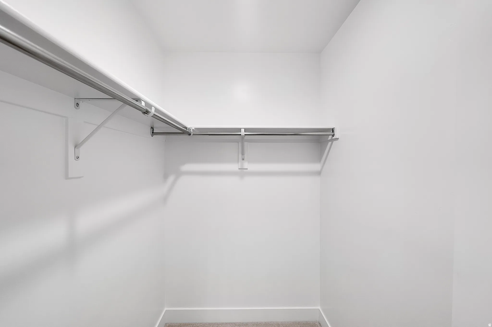 Walk-in closet with white walls, L-shaped shelving, and metal hanging rods. This is not the actual home being built but a representation of the features available in this home. Colors and finishes may differ from those shown.