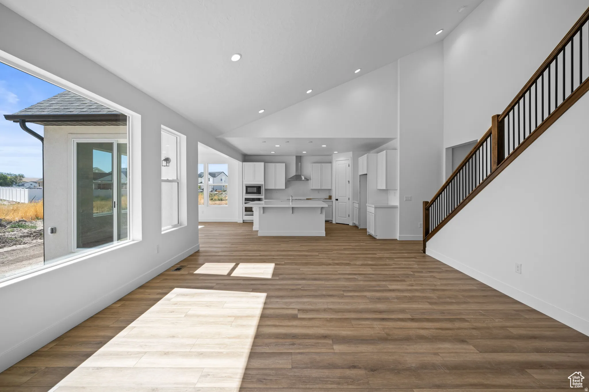 Open-concept main living area featuring wood-finish flooring, high vaulted ceilings with recessed lighting, and a contemporary staircase. This is not the actual home being built but a representation of the features available in this home. Colors and finis