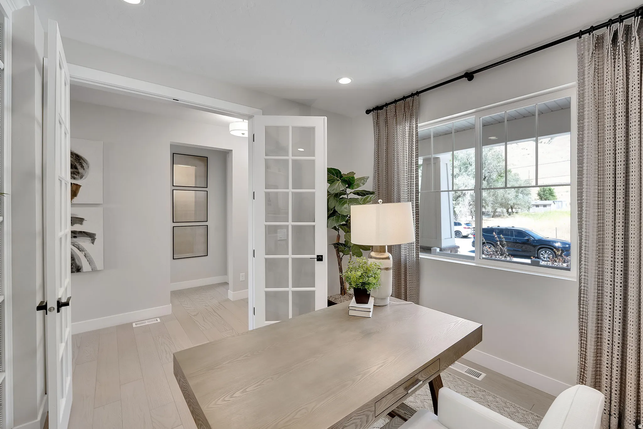 French doors with clear glass panels open to a bright room featuring wood-finish flooring, recessed lighting, and a large multi-pane window. This is not the actual home being built but a representation of the features available in this home. Colors and fi