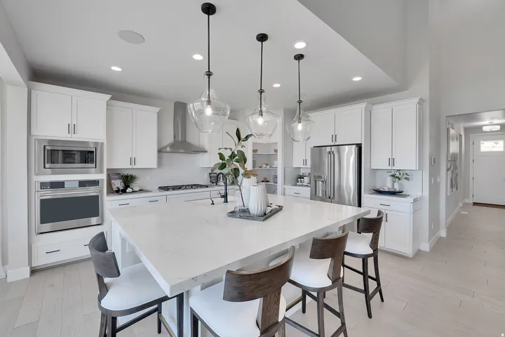 Bright kitchen featuring a large central island with seating, white shaker cabinetry, stainless steel appliances, and wood-finish flooring.