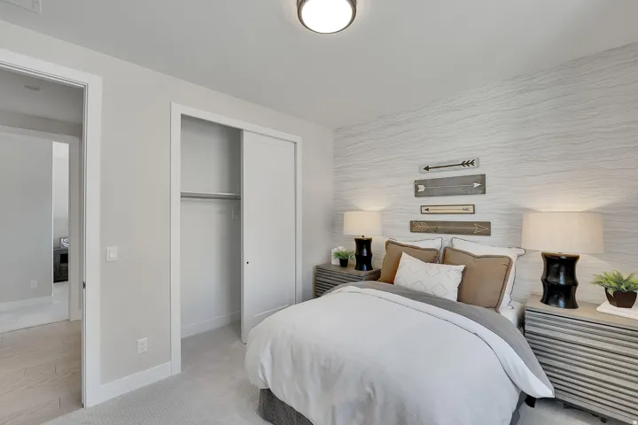 Bedroom featuring a patterned accent wall, light gray carpeting, and a built-in closet with sliding doors. This is not the actual home being built but a representation of the features available in this home. Colors and finishes may differ from those shown